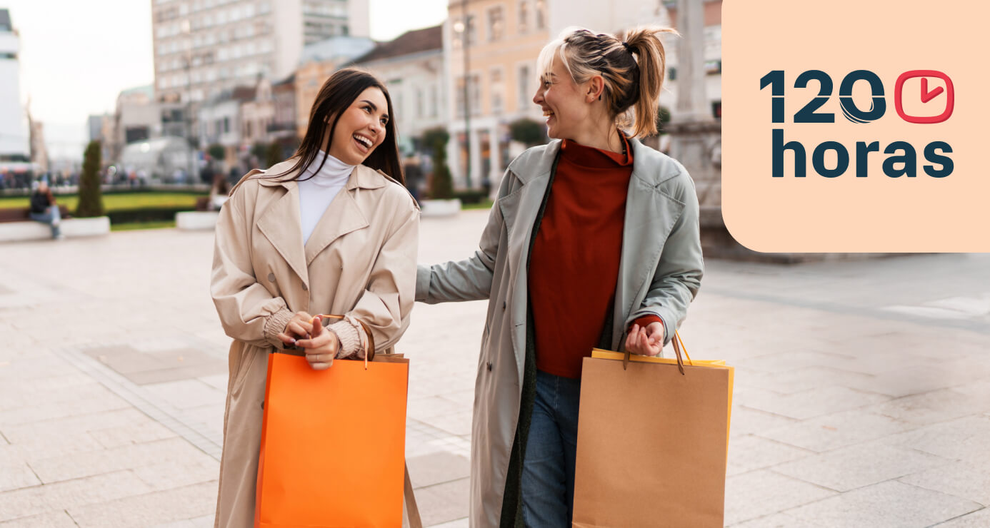 Dos mujeres sonrientes cargando bolsas, disfrutando de una tarde de compras.