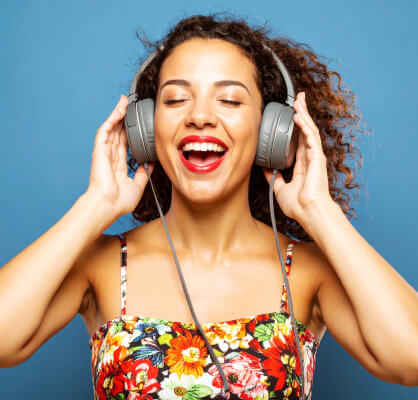 Una mujer con los ojos cerrados disfrutando música mientras sostiene sus audífonos.