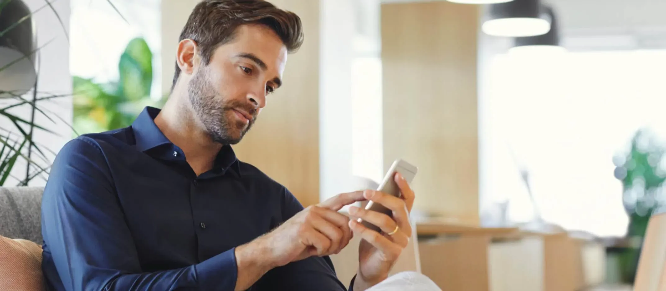 Persona consultando información financiera en smartphone mientras está sentado en una sala moderna, representando búsqueda de Afore.