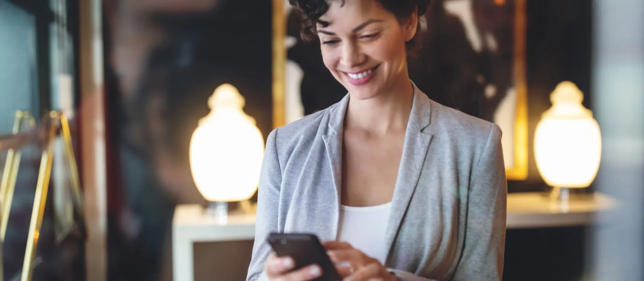 Persona sosteniendo un teléfono móvil en un entorno elegante con lámparas decorativas, representando consulta del estado de cuenta Afore desde el celular.