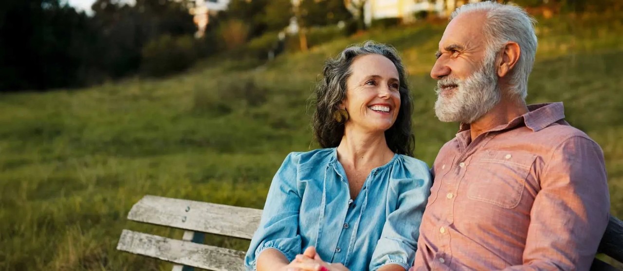Pareja sentada en una banca de madera en un parque al aire libre durante el atardecer.
