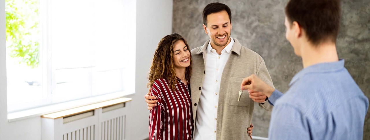 Pareja recibiendo las llaves de una vivienda nueva de parte de un agente en un espacio interior iluminado.