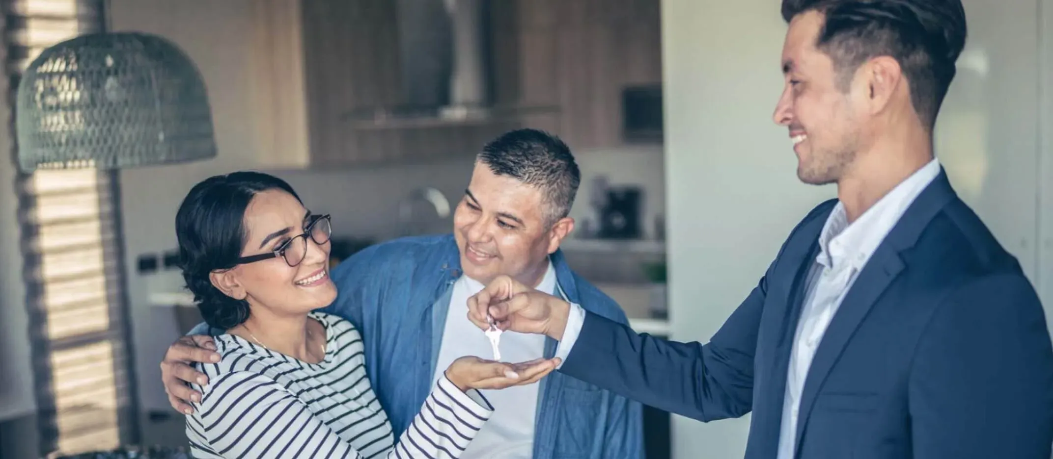 Persona entregando llaves a una pareja dentro de una casa, representando la compra de vivienda y elección del plazo correcto para un crédito hipotecario.