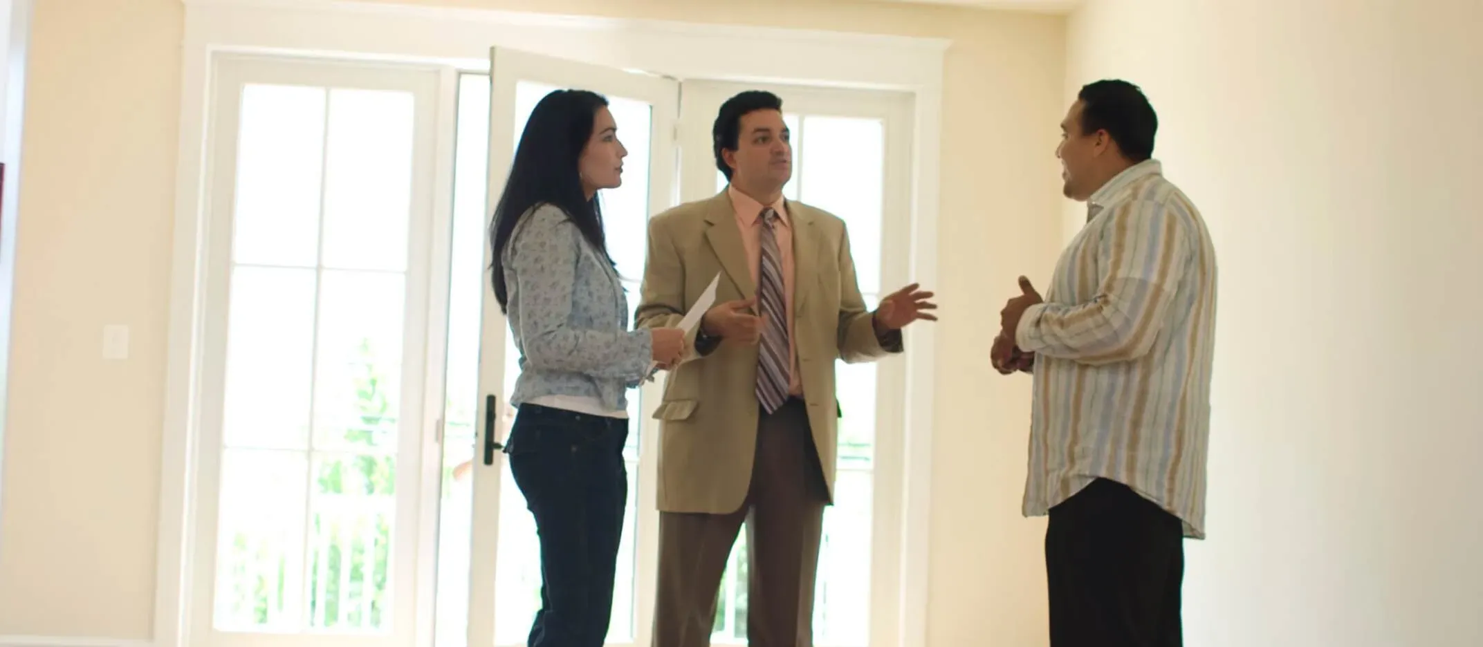 Tres personas conversando dentro de una vivienda vacía, con luz natural entrando por puertas de vidrio, representando asesoría inmobiliaria para comprar una casa.