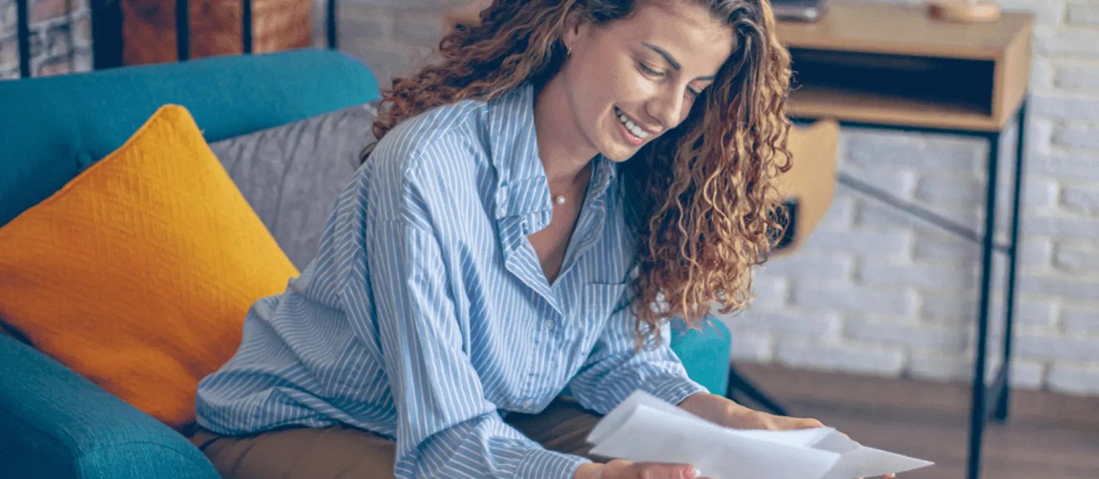 Persona sentada en un sillón azul con cojín amarillo, sosteniendo documentos y revisando información financiera.