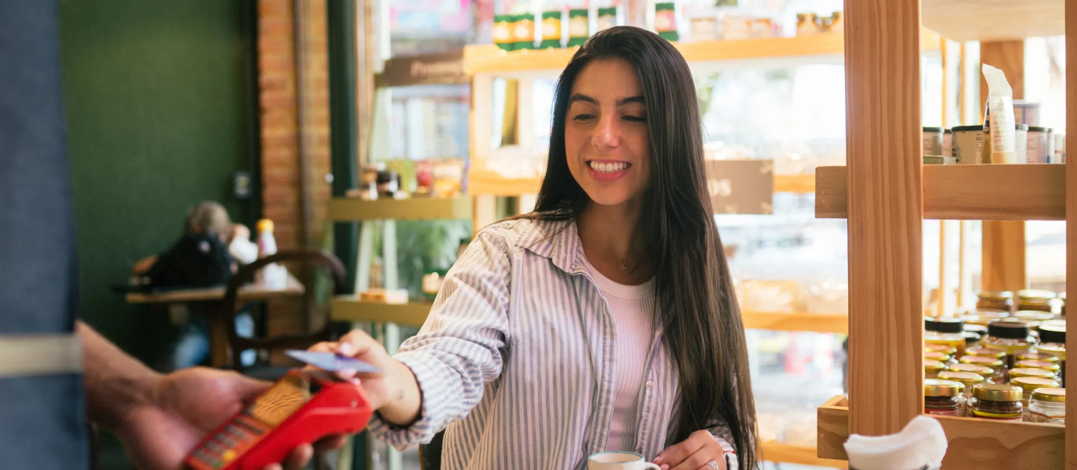 Una mujer pagando con una tarjeta contactless en una terminal de pago en una cafetería.