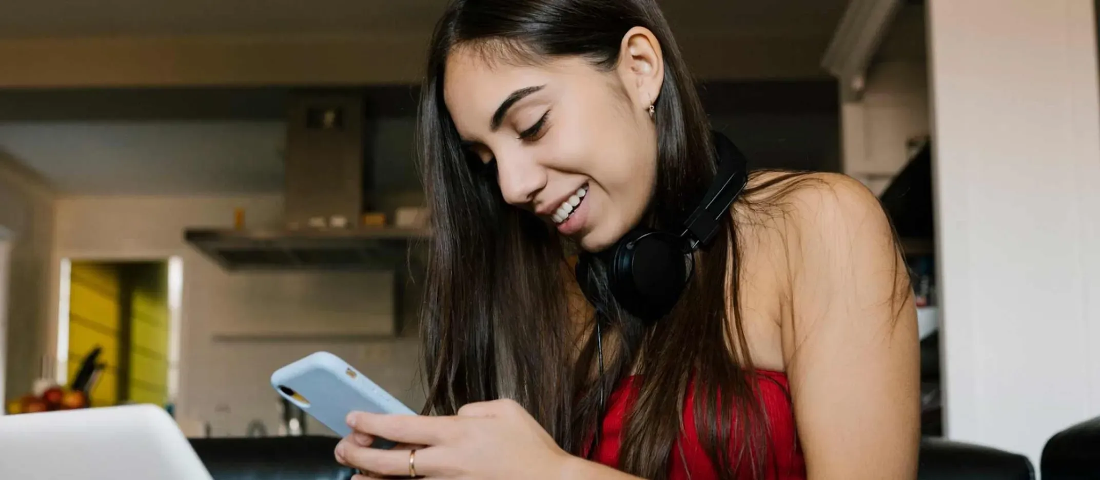 Persona sentada frente a una computadora portátil sosteniendo un teléfono móvil.