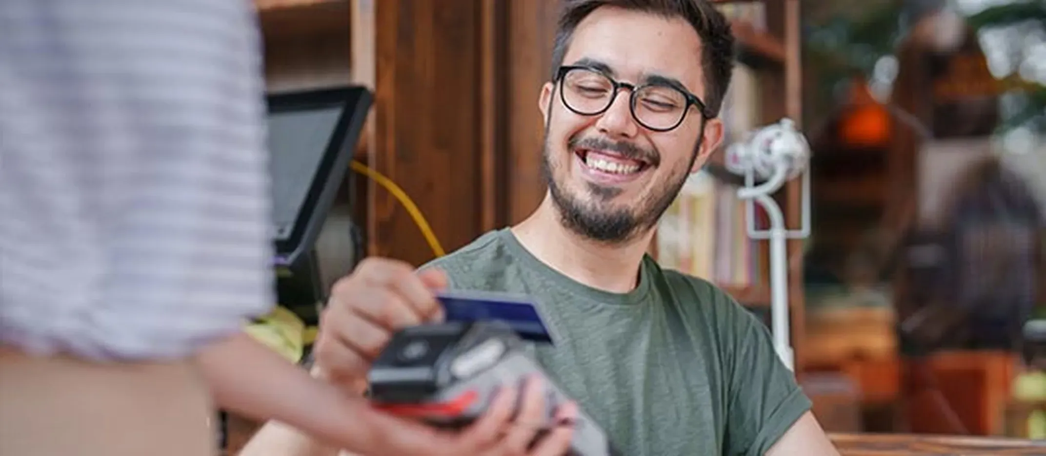 Persona pagando con tarjeta de débito en un lector de pagos en establecimiento.
