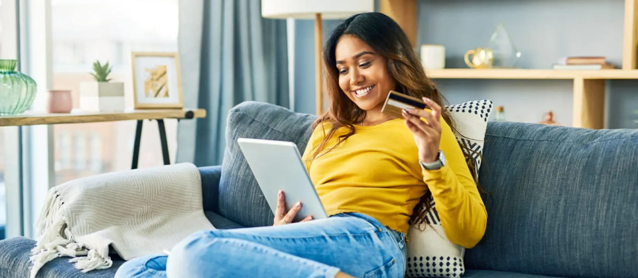 Persona comprando en línea con tarjeta de débito y tablet desde su sala.