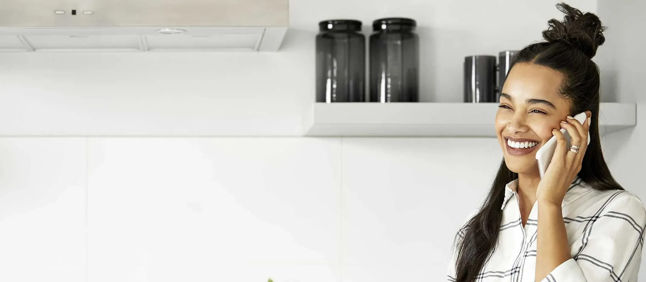 Persona realizando llamada telefónica en cocina moderna con estantes y frascos decorativos.