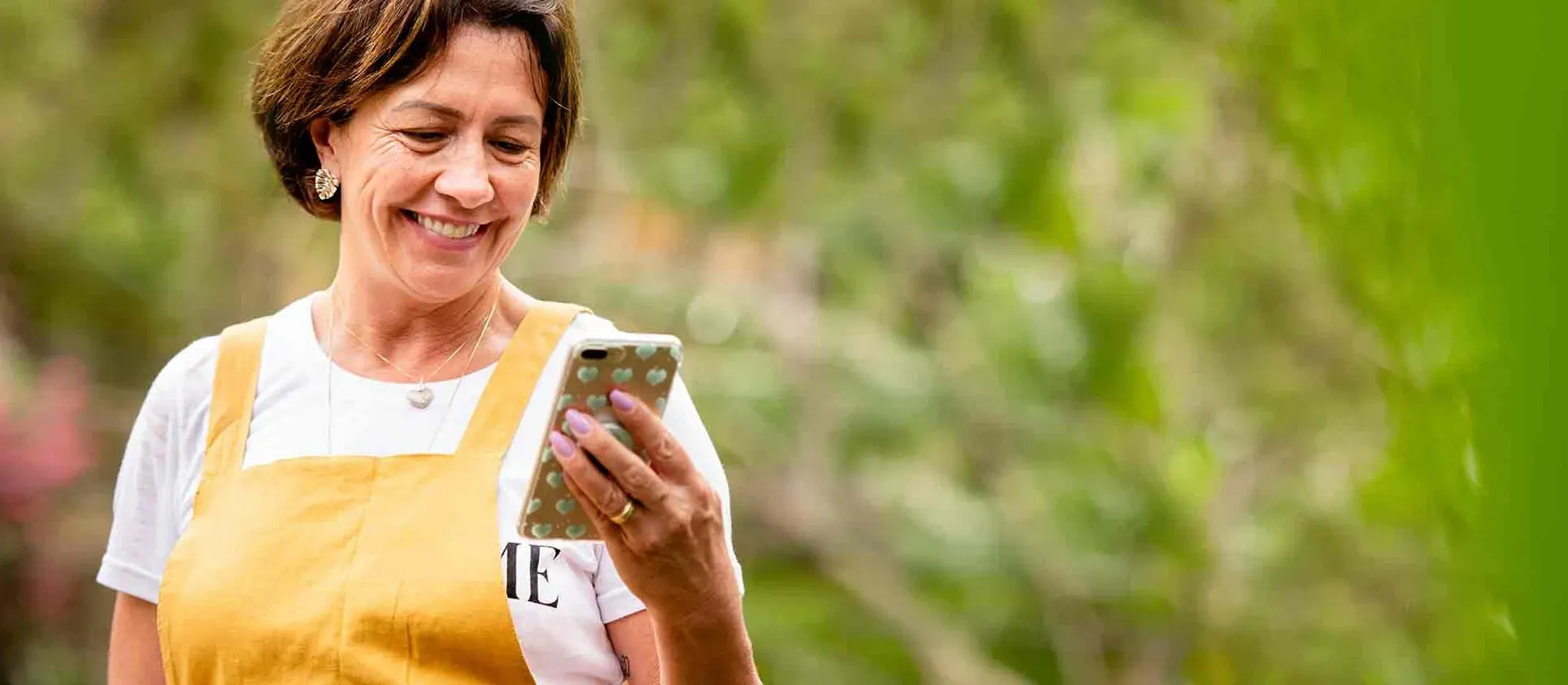 Persona sosteniendo un teléfono móvil con funda decorativa, realizando operación bancaria en espacio exterior con vegetación.