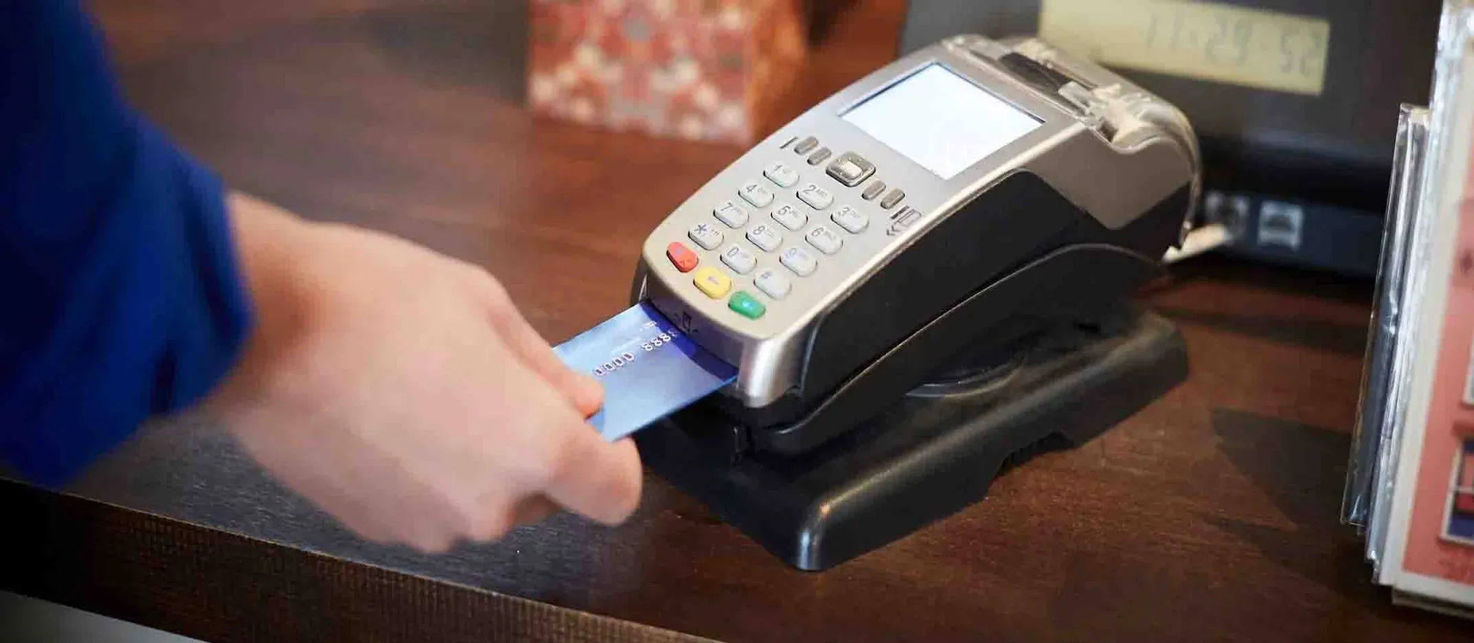 Mano insertando tarjeta de crédito en terminal punto de venta sobre mostrador de madera.