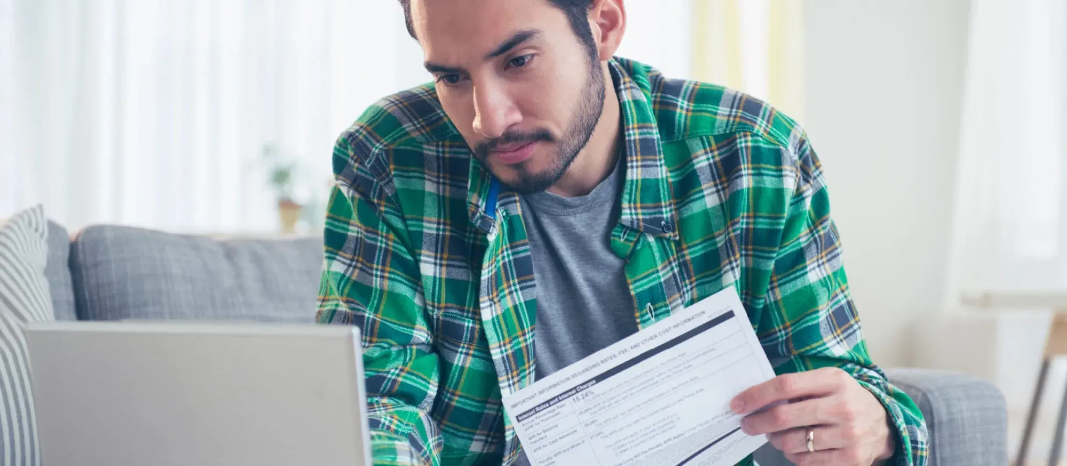 Persona sentada en un sofá revisando documentos financieros mientras utiliza una computadora portátil, representando análisis de gastos y control de finanzas personales.