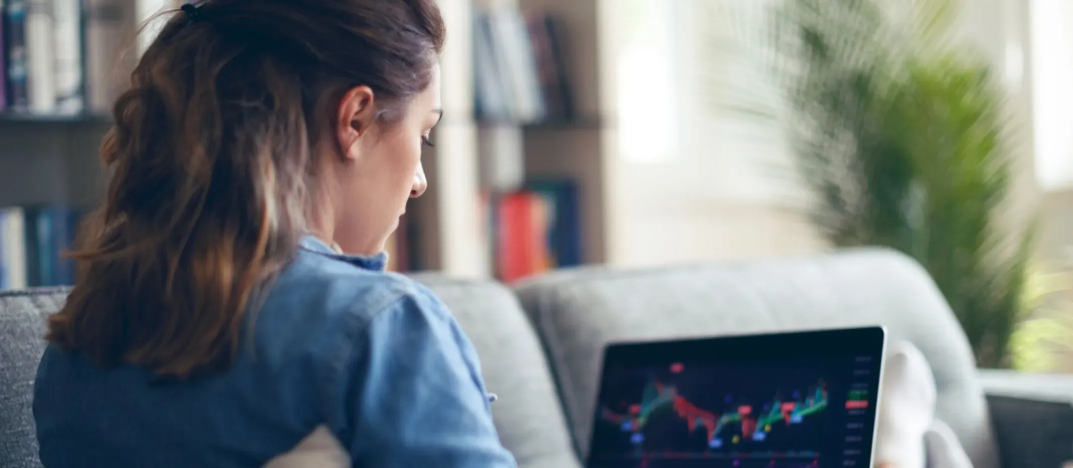 Persona sentada en un sofá revisando gráficos financieros en una computadora portátil, representando análisis de inversiones y estrategias para principiantes.