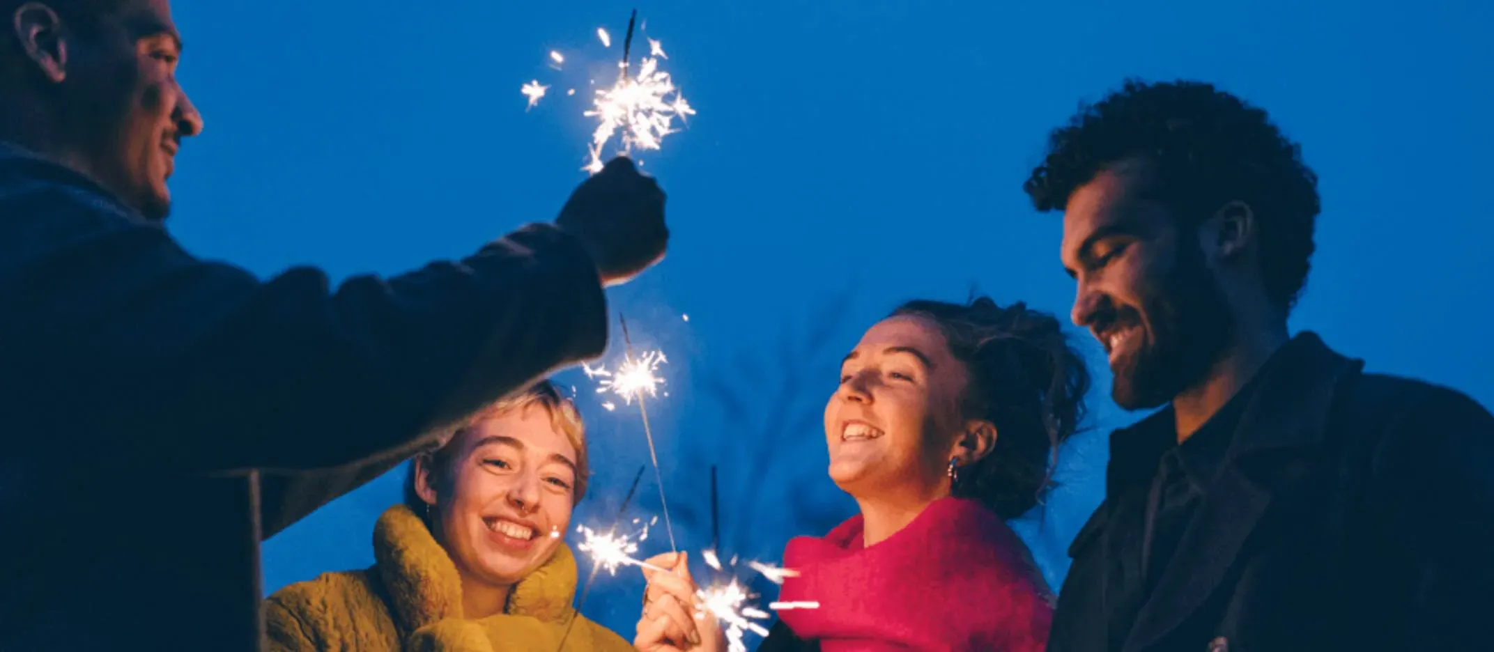 Grupo de personas sosteniendo bengalas encendidas al aire durante una celebración nocturna, representando inicio de año y consejos para sobrevivir la cuesta de enero.