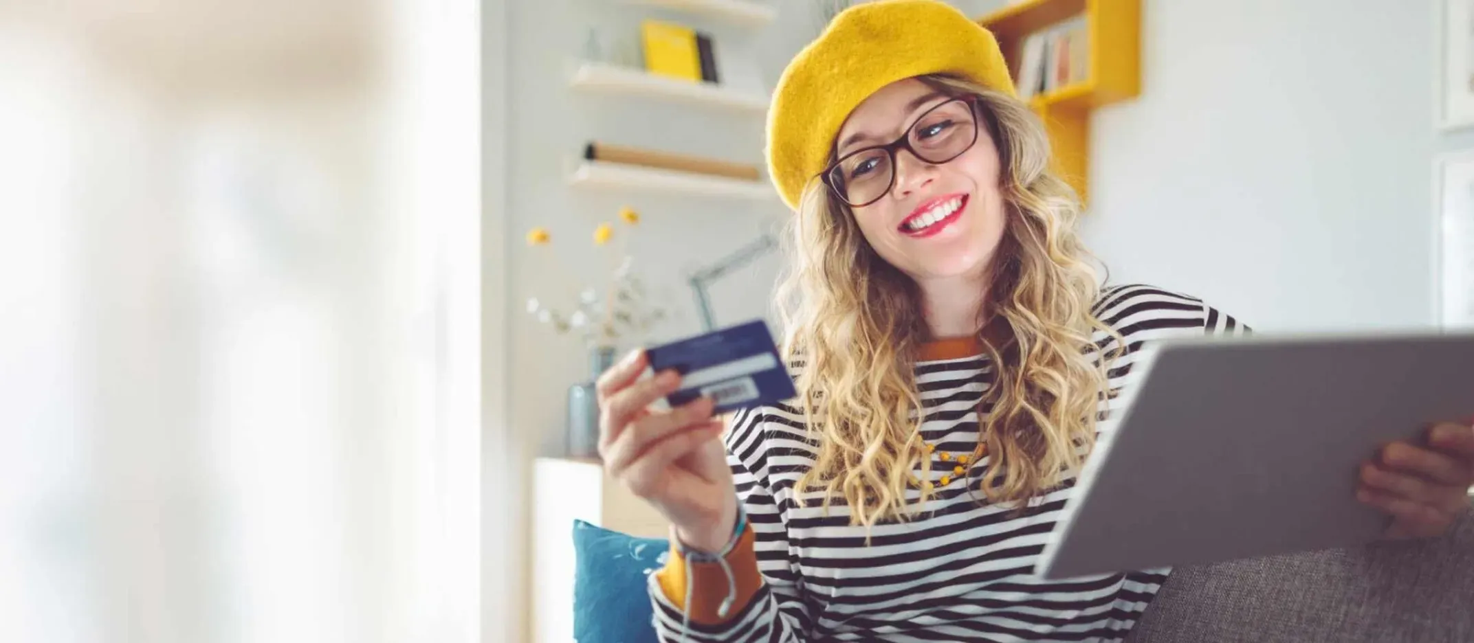 Persona sosteniendo tarjeta bancaria y tablet mientras realiza trámites desde casa.