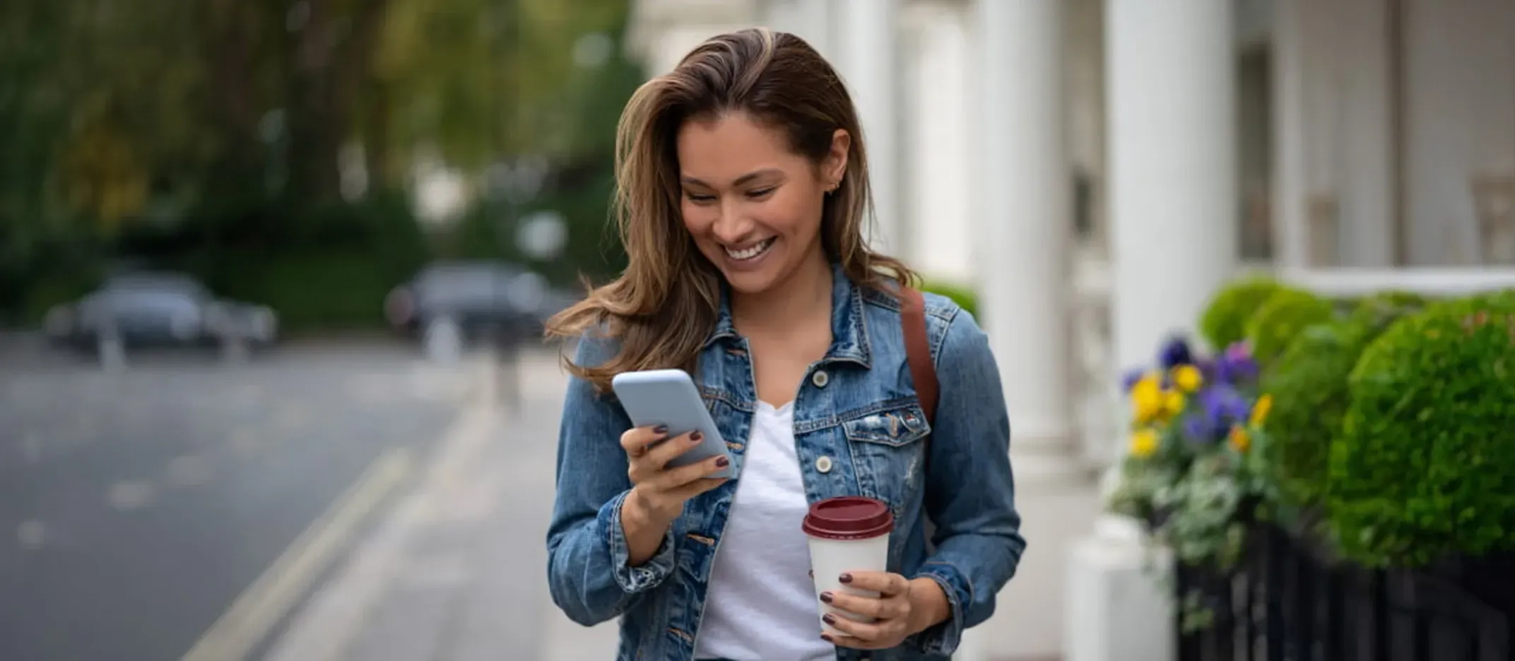 Persona caminando por la calle mientras sostiene un teléfono móvil y un vaso de café.