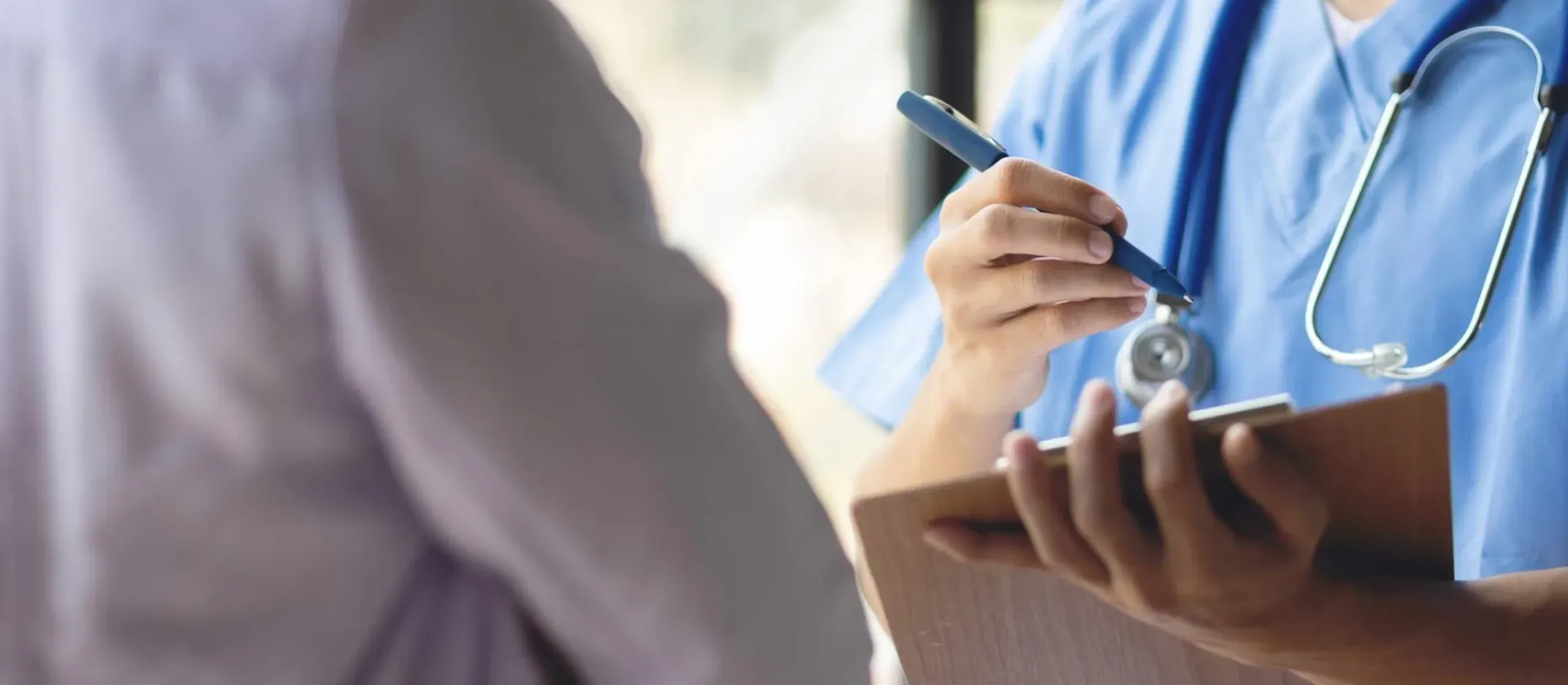 Profesional de salud escribiendo en portapapeles durante consulta médica.