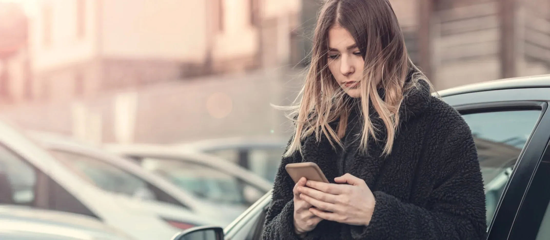 Persona de pie junto a un automóvil en estacionamiento usando un teléfono móvil.