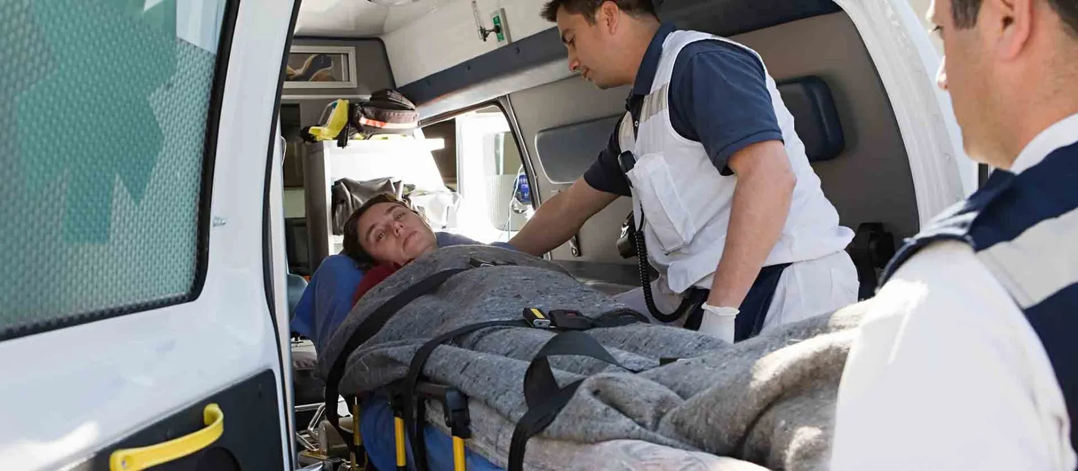 Paramédicos atendiendo a una persona en camilla dentro de una ambulancia durante una emergencia médica.