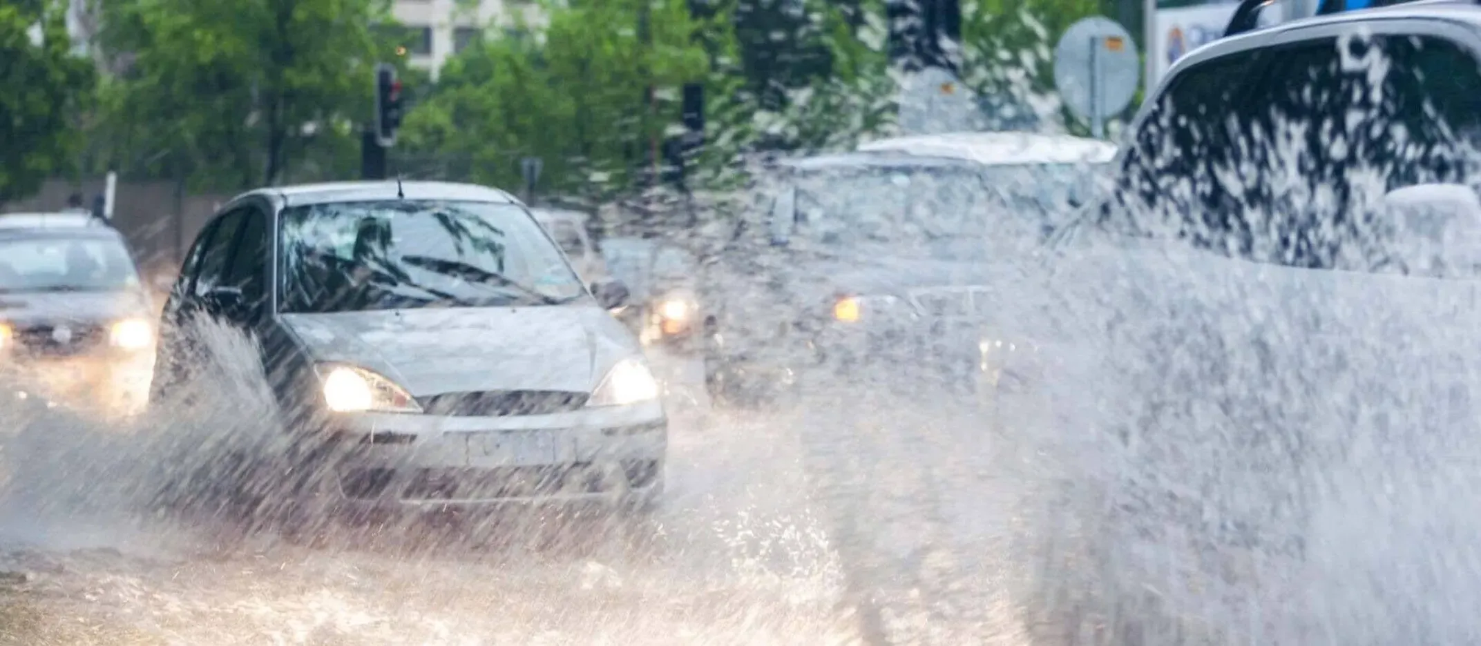 Automóviles circulando por una calle inundada con agua salpicando tras fuertes lluvias.