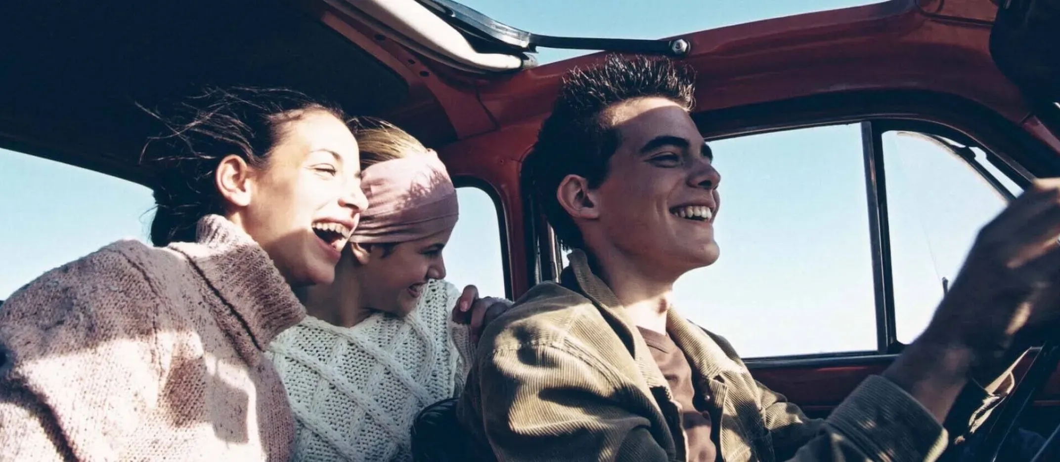 Personas viajando en auto clásico por carretera bajo cielo despejado.