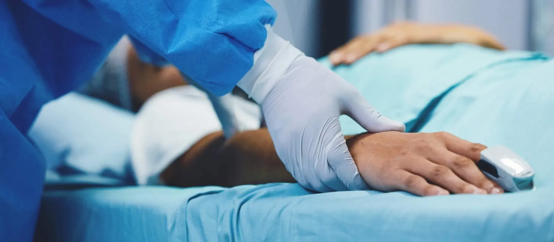 Profesional de salud revisando la mano de un paciente hospitalizado en cama.