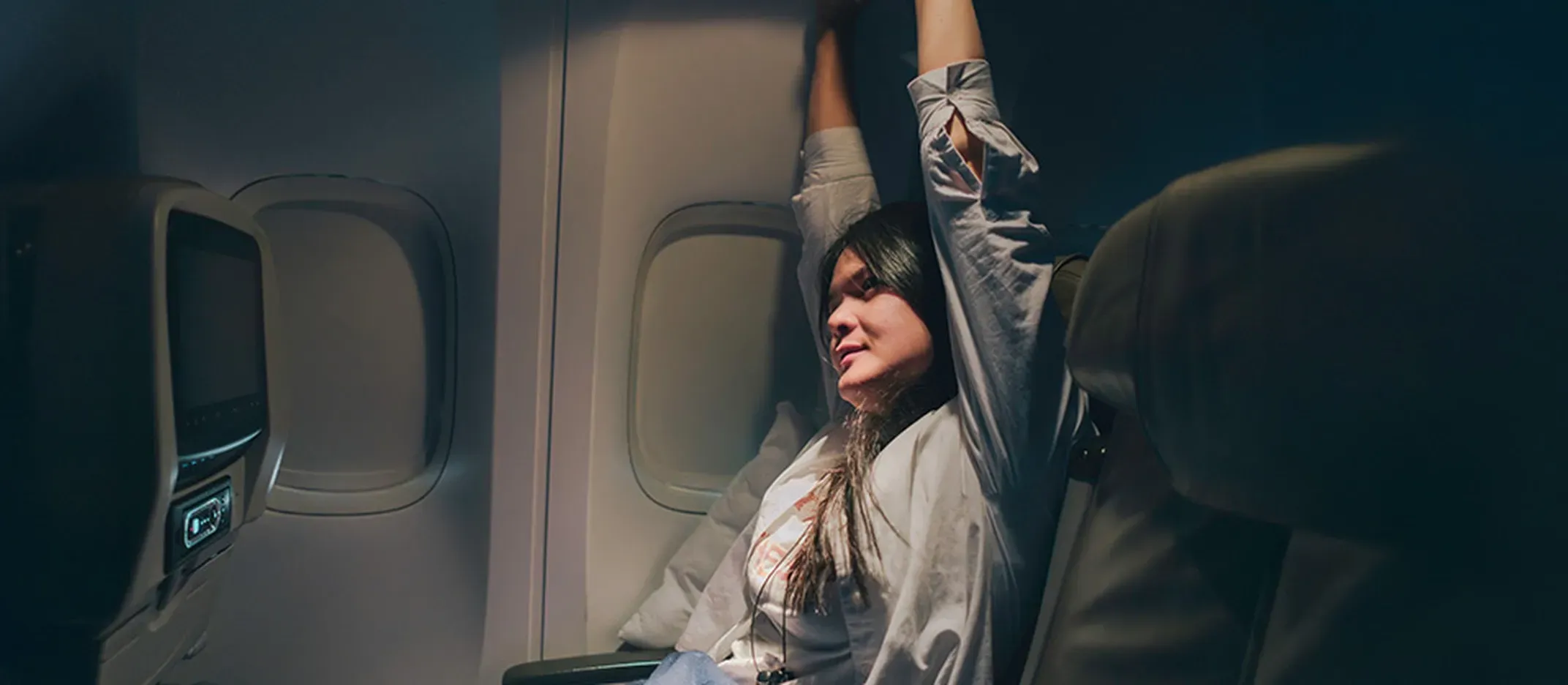 Persona sentada en asiento de avión estirando los brazos durante un vuelo nocturno.