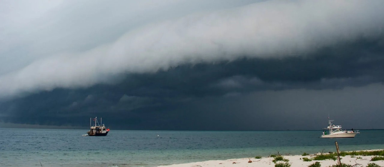 Dos embarcaciones en el mar cerca de la costa con una gran nube de tormenta en el horizonte.