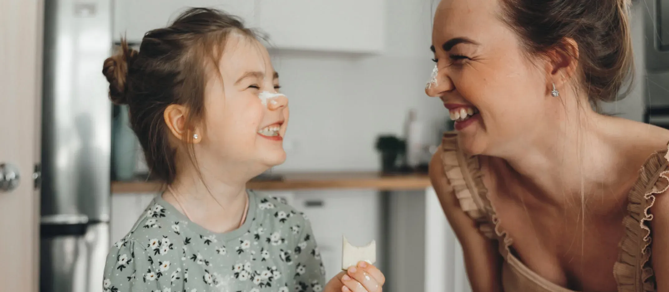 Persona adulta conversando con menor en cocina moderna mientras sostiene un alimento.