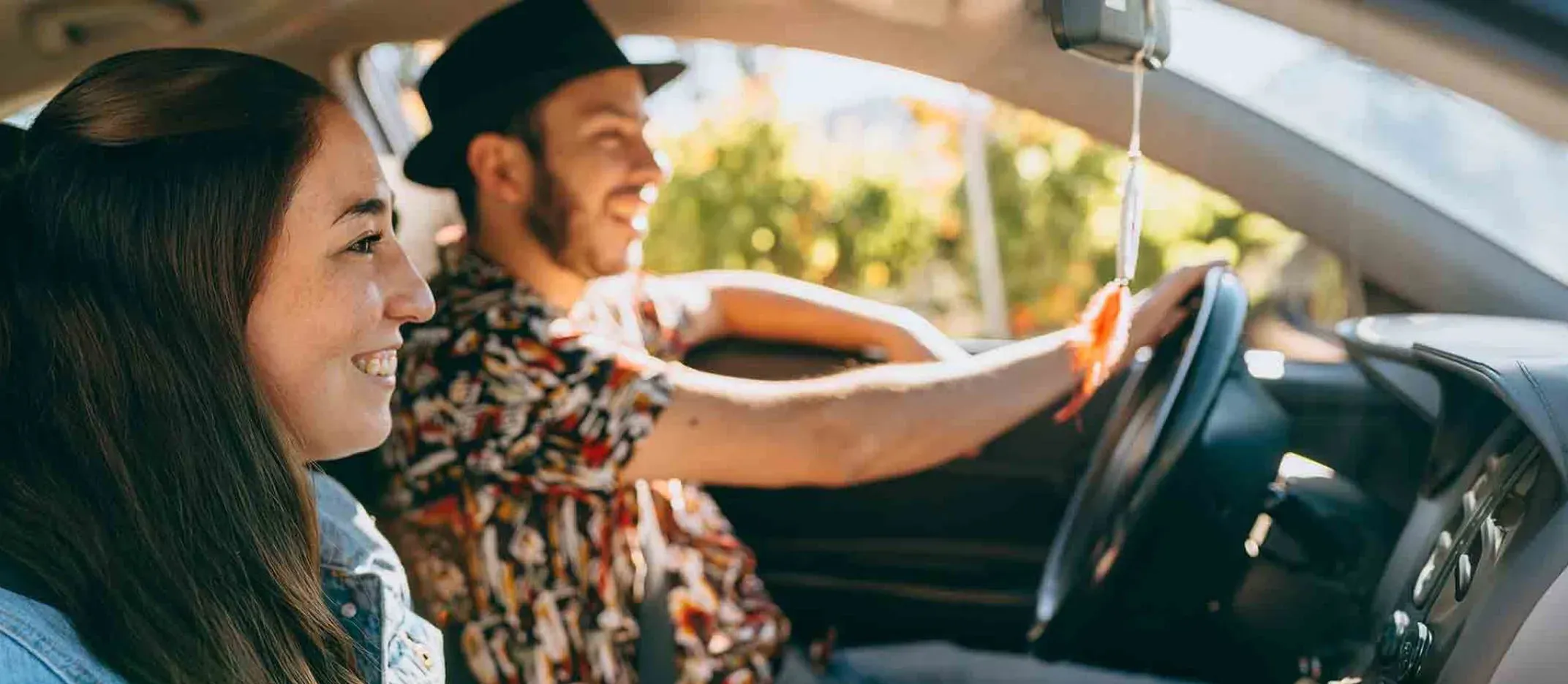 Dos personas viajando en auto, conductor al volante y pasajero en asiento delantero durante el día.