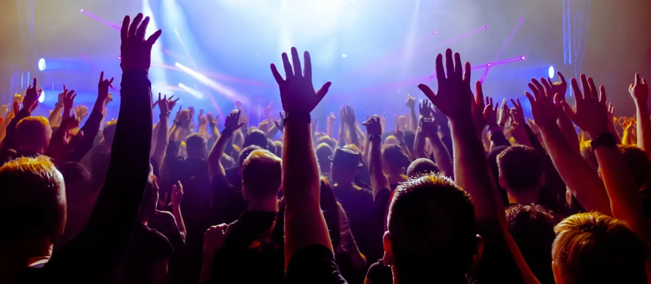Personas levantando las manos en un concierto con luces de colores en el escenario.