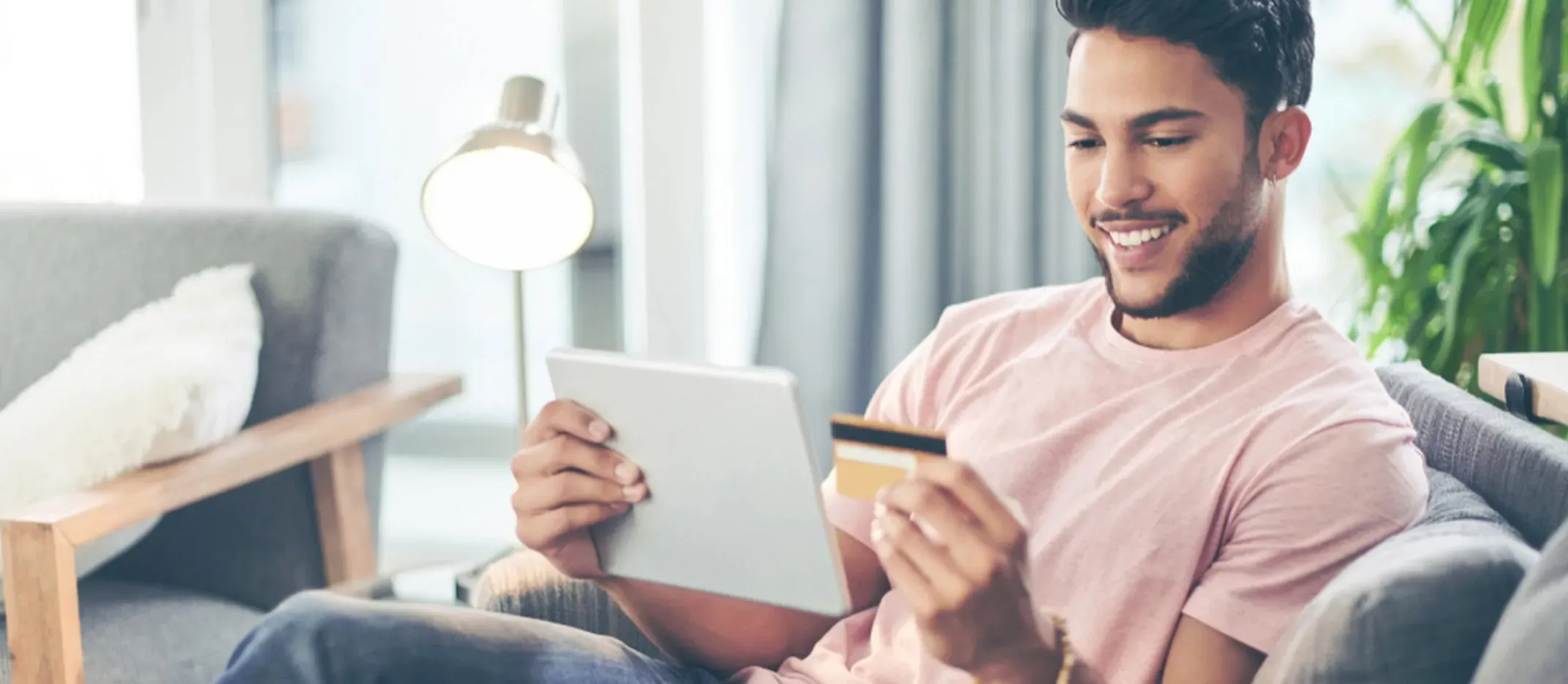 Persona sentada en un sillón sosteniendo una tarjeta de crédito y una tablet.