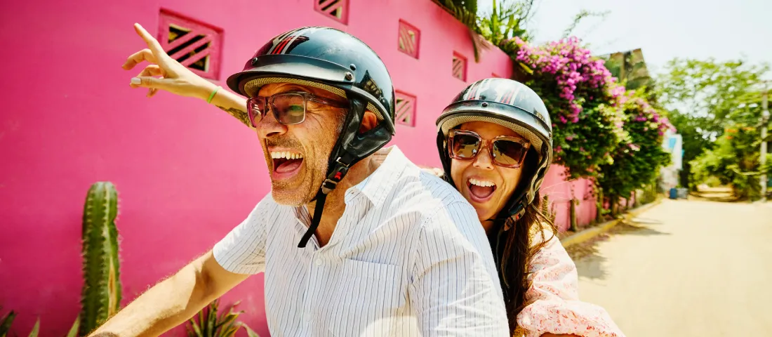 Personas con cascos recorren una calle colorida durante un viaje vacacional, ilustrando cómo viajar con puntos y ahorrar en vacaciones aprovechando beneficios de tarjeta.
