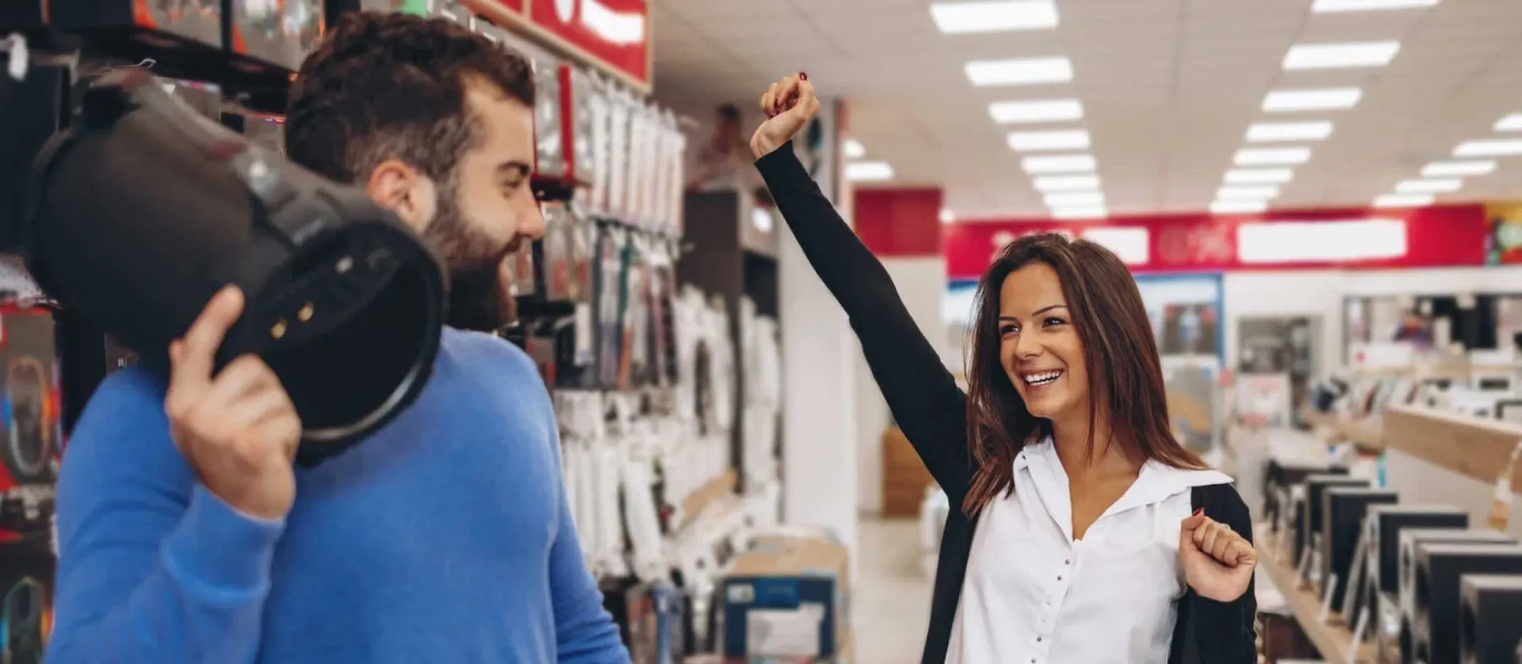 Personas en tienda de electrónicos celebrando compra durante temporada de ofertas.