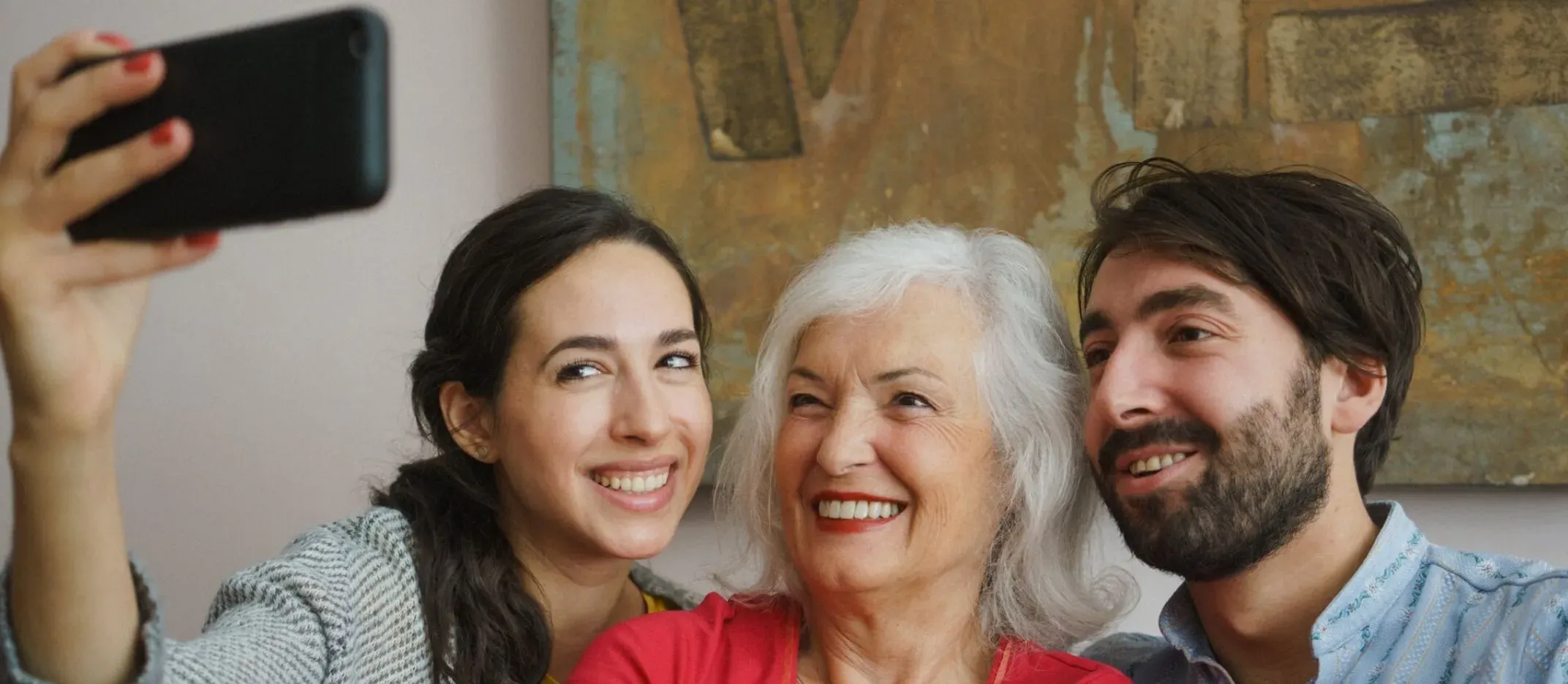 Tres personas tomando una selfie con un teléfono móvil en una sala con cuadro decorativo.