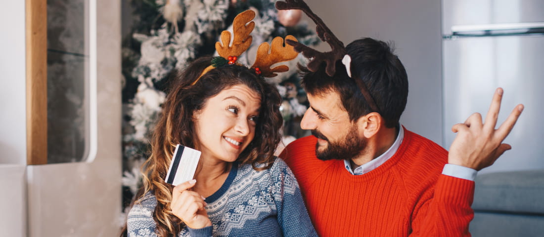 Pareja de hombre y mujer vestidos con sueter navideño mostrando una tarjeta