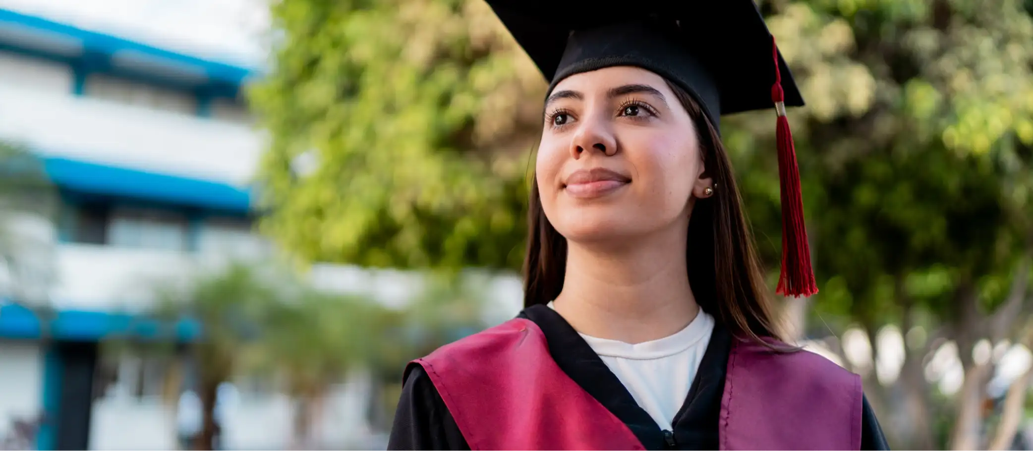 Mujer con toga y birrete de graduación con borla roja posa al aire libre, programa de Educación Financiera Banamex
