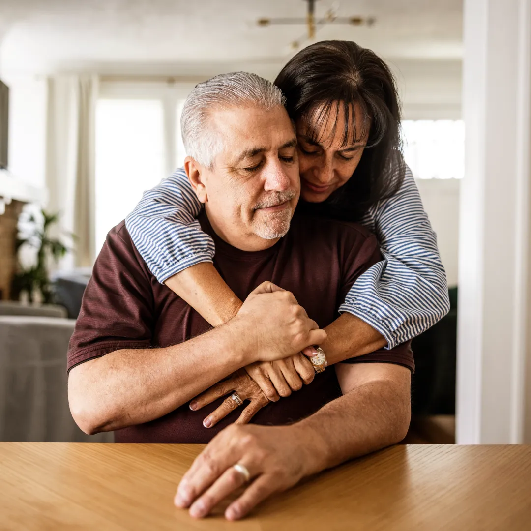 Pareja adulta compartiendo un abrazo en el hogar, reflejando bienestar, tranquilidad y estabilidad para disfrutar una vida en común.