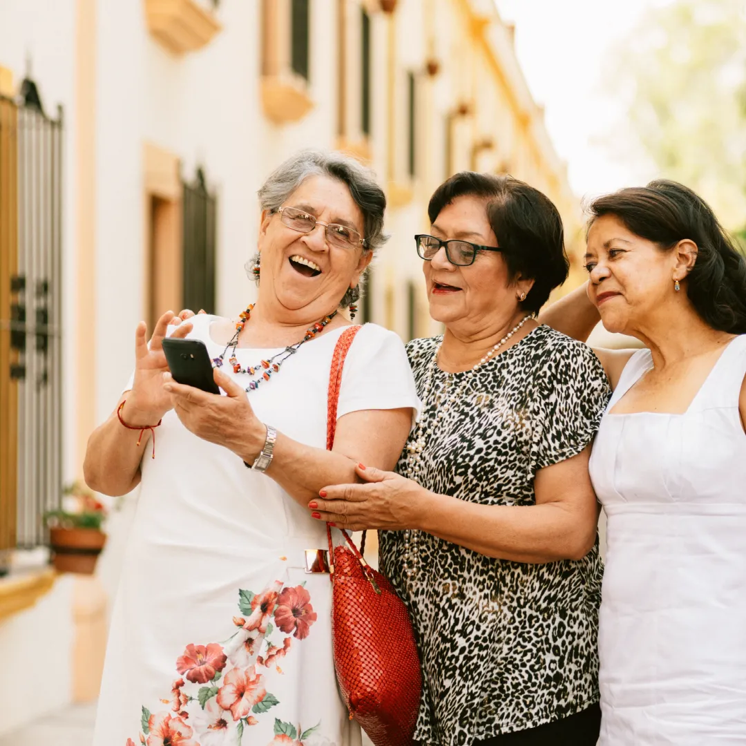 Personas adultas compartiendo un momento de convivencia en la vía pública mientras consultan información desde un teléfono móvil.