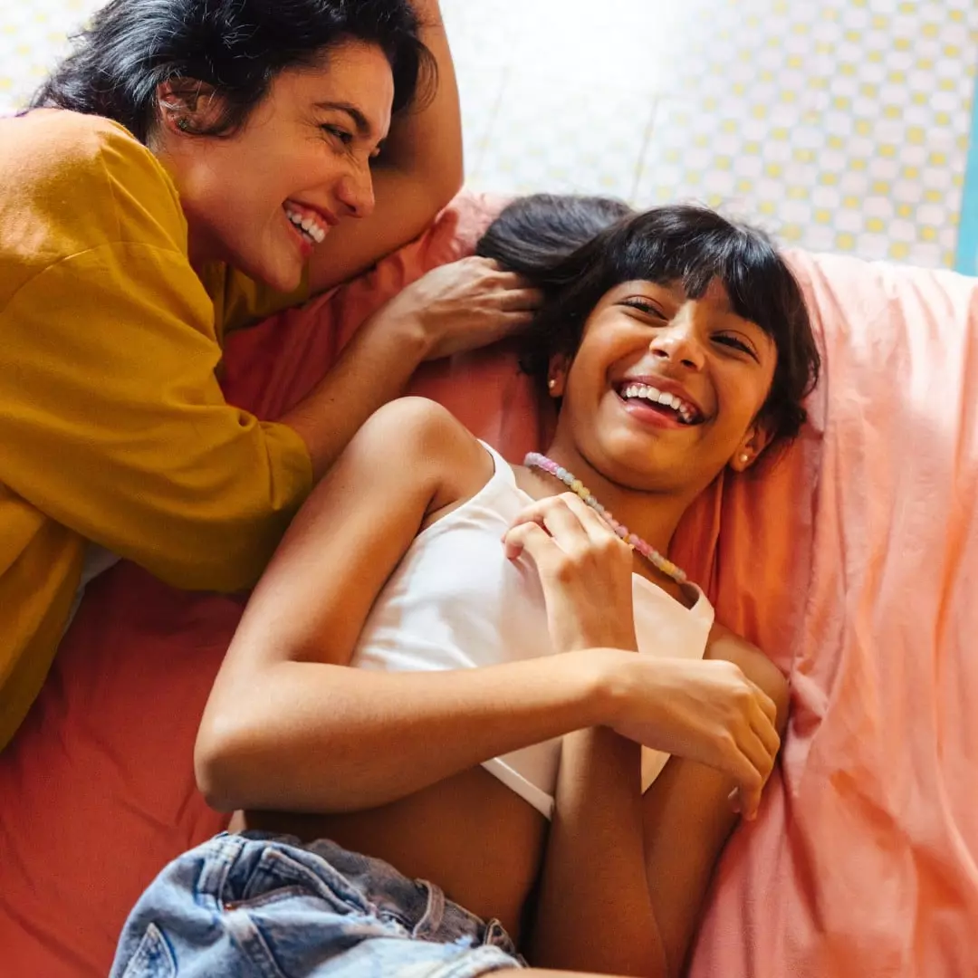 Madre adulta y su hijo compartiendo tiempo en casa sobre una cama, representando bienestar familiar, protección financiera y la tranquilidad de planear el futuro con Banamex.