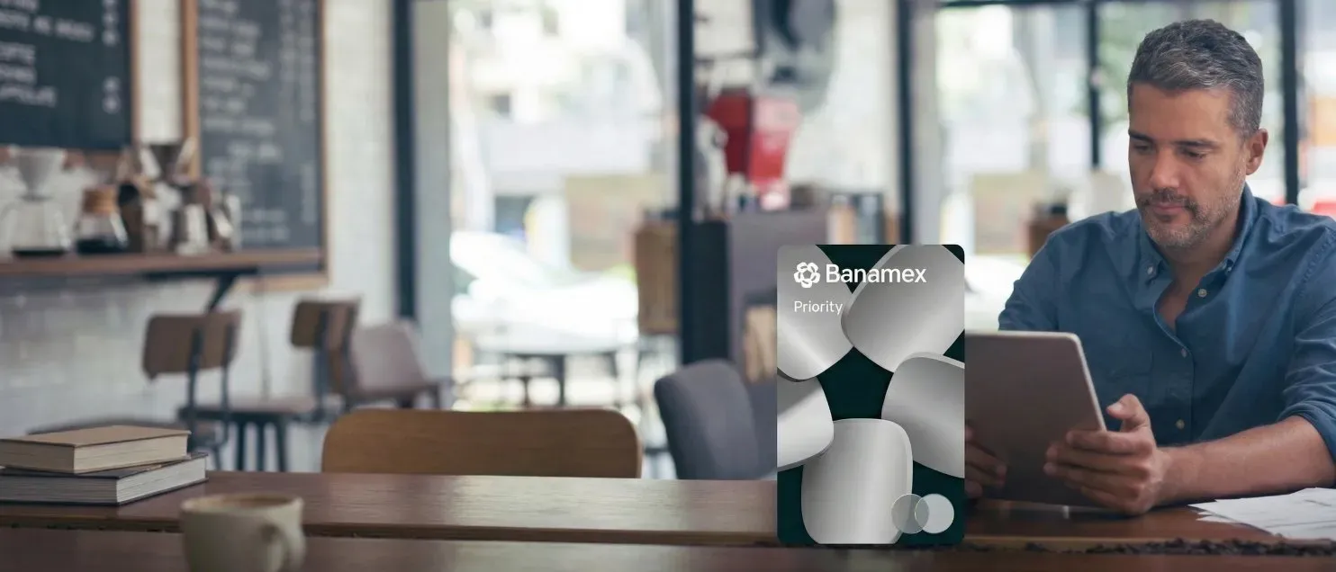 Un hombre en una cafetería usando un celular junto a la tarjeta Priority Banamex.