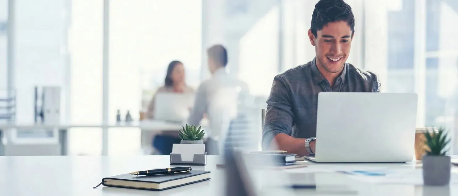 Persona trabajando en una computadora portátil en una mesa con documentos y bolígrafo.