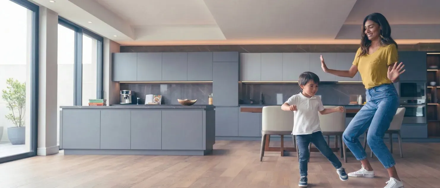 Adulto y menor bailando en una sala moderna con piso de madera, simbolizando bienestar y estabilidad financiera tras adquirir una vivienda con crédito hipotecario.
