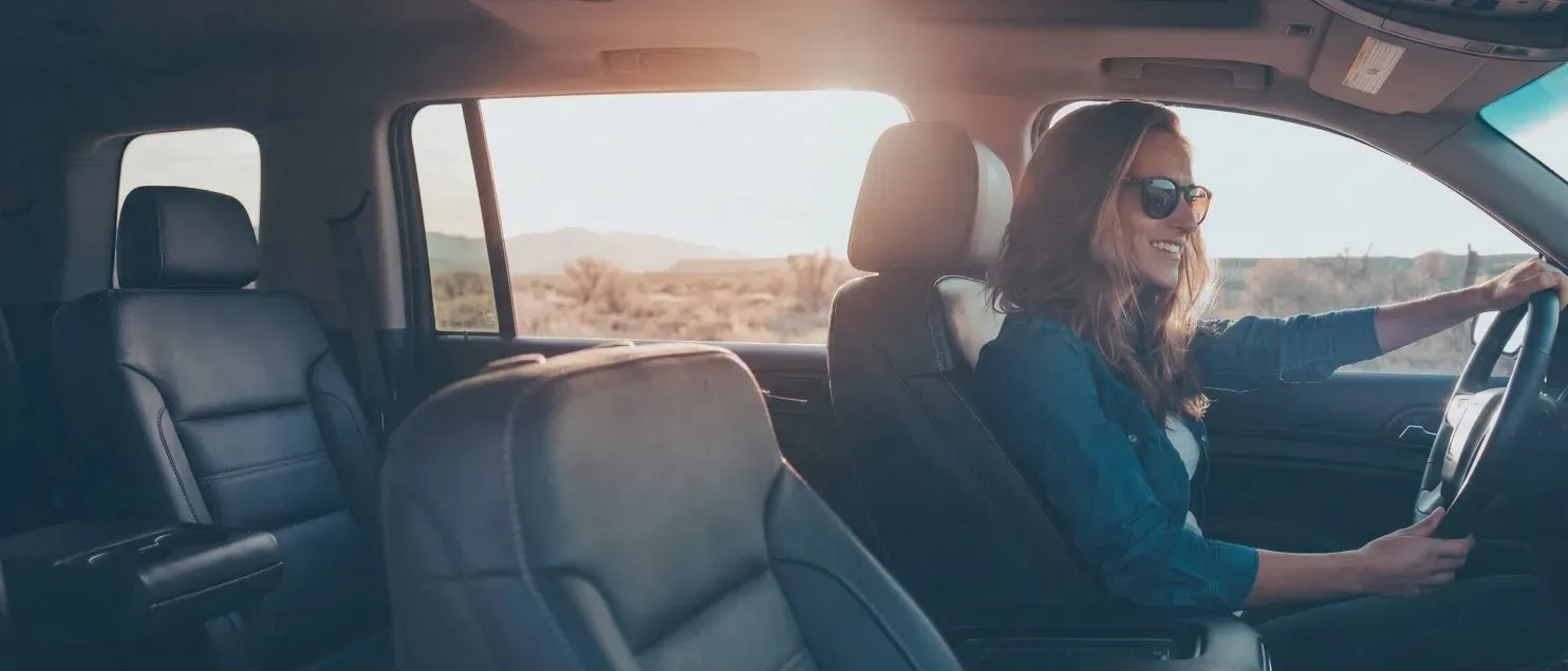 Una mujer conduciendo un automóvil en una carretera con paisaje desértico al fondo.