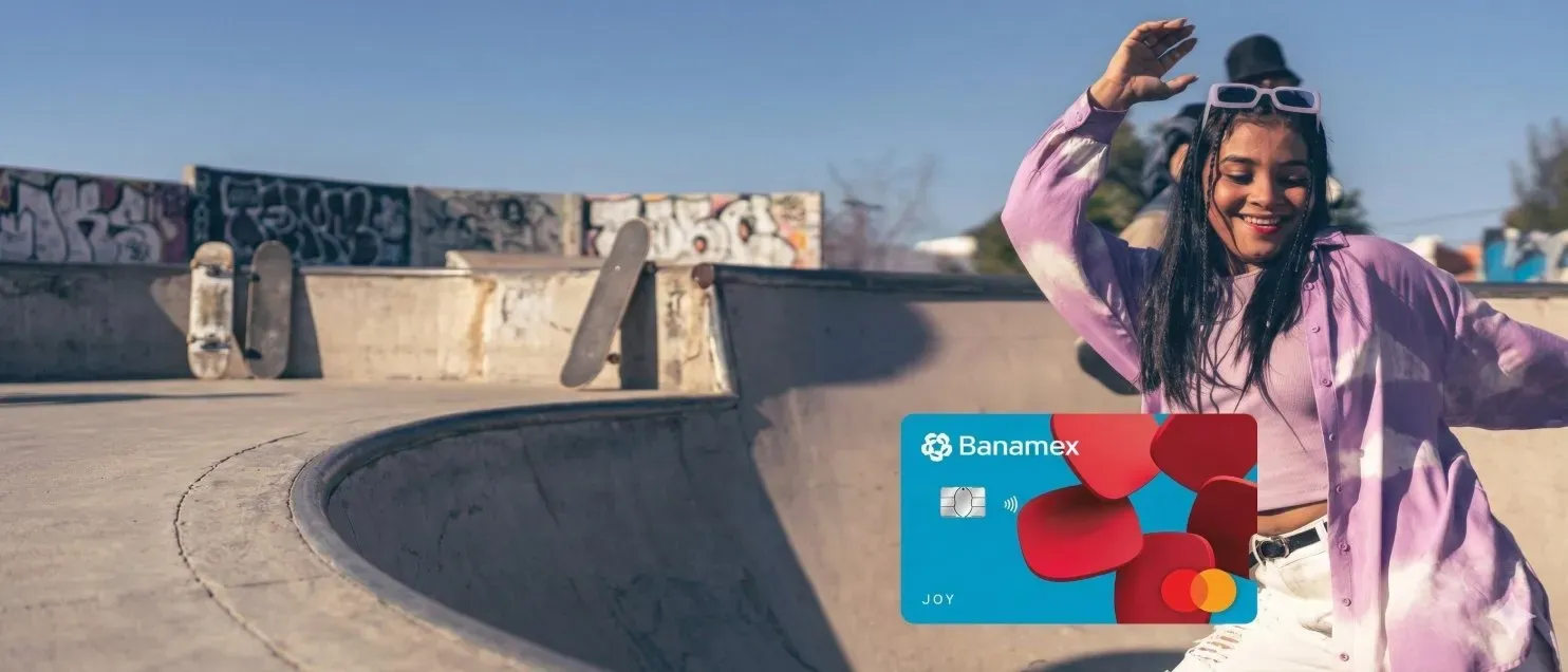 Una joven en una pista de skate levantando los brazos junto a la Tarjeta de Crédito Joy Banamex.