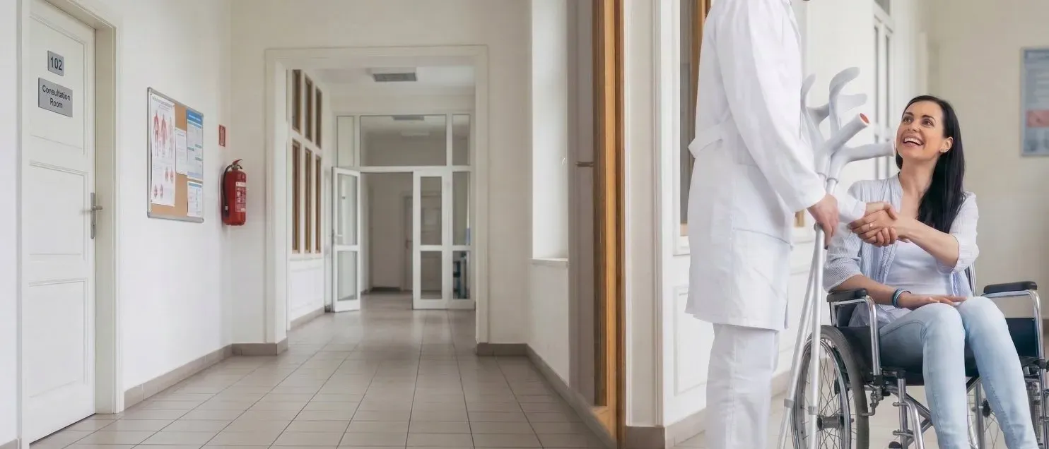 Una mujer sentada en una silla de ruedas estrechando la mano de un doctor en un pasillo de hospital.