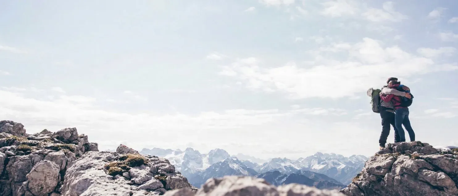 Pareja abrazada en la cima de una montaña con mochilas, simbolizando libertad financiera y metas alcanzadas para el retiro.
