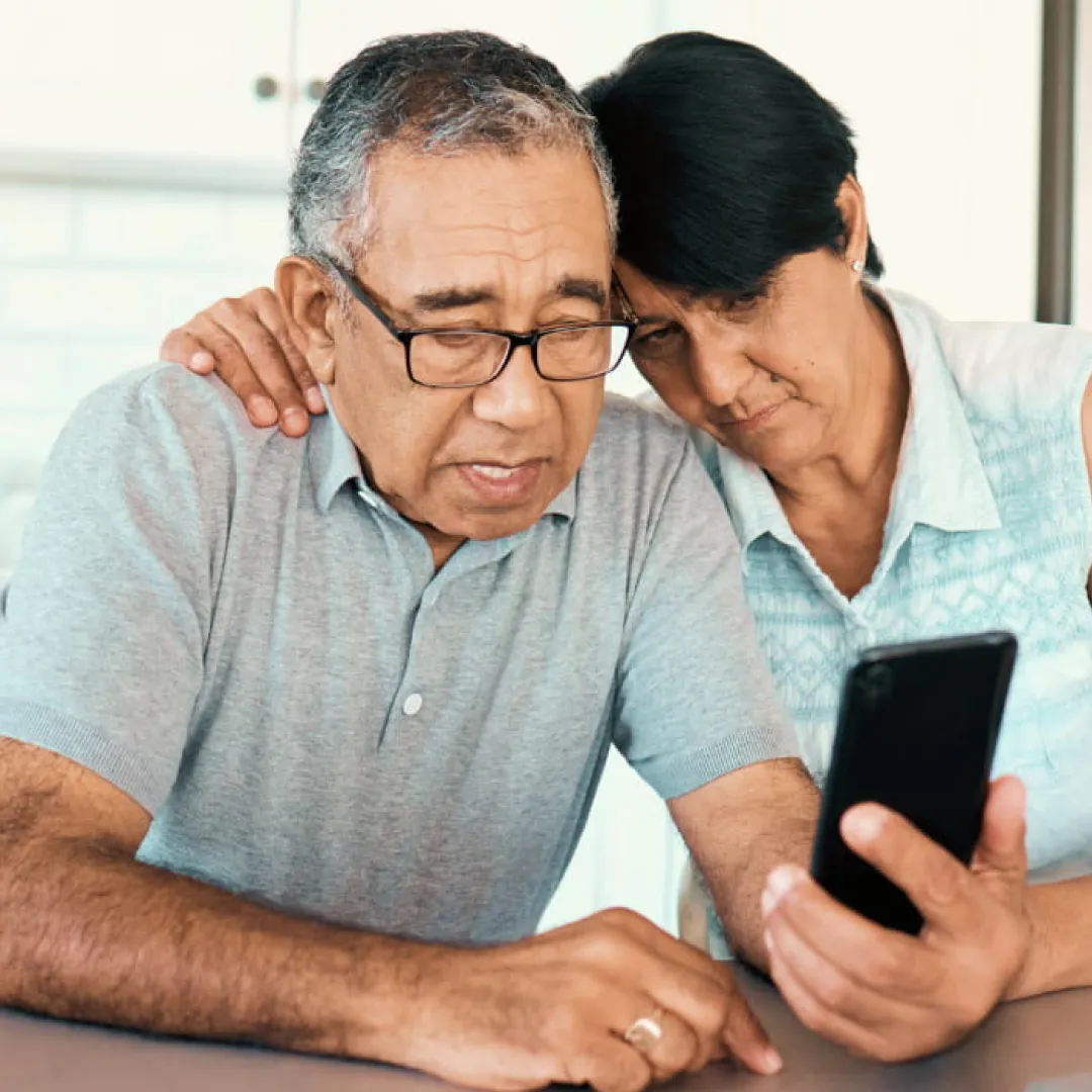 Dos personas adultas consultando información en un teléfono móvil desde casa, representando el uso de servicios digitales y la gestión segura de finanzas con Banamex.