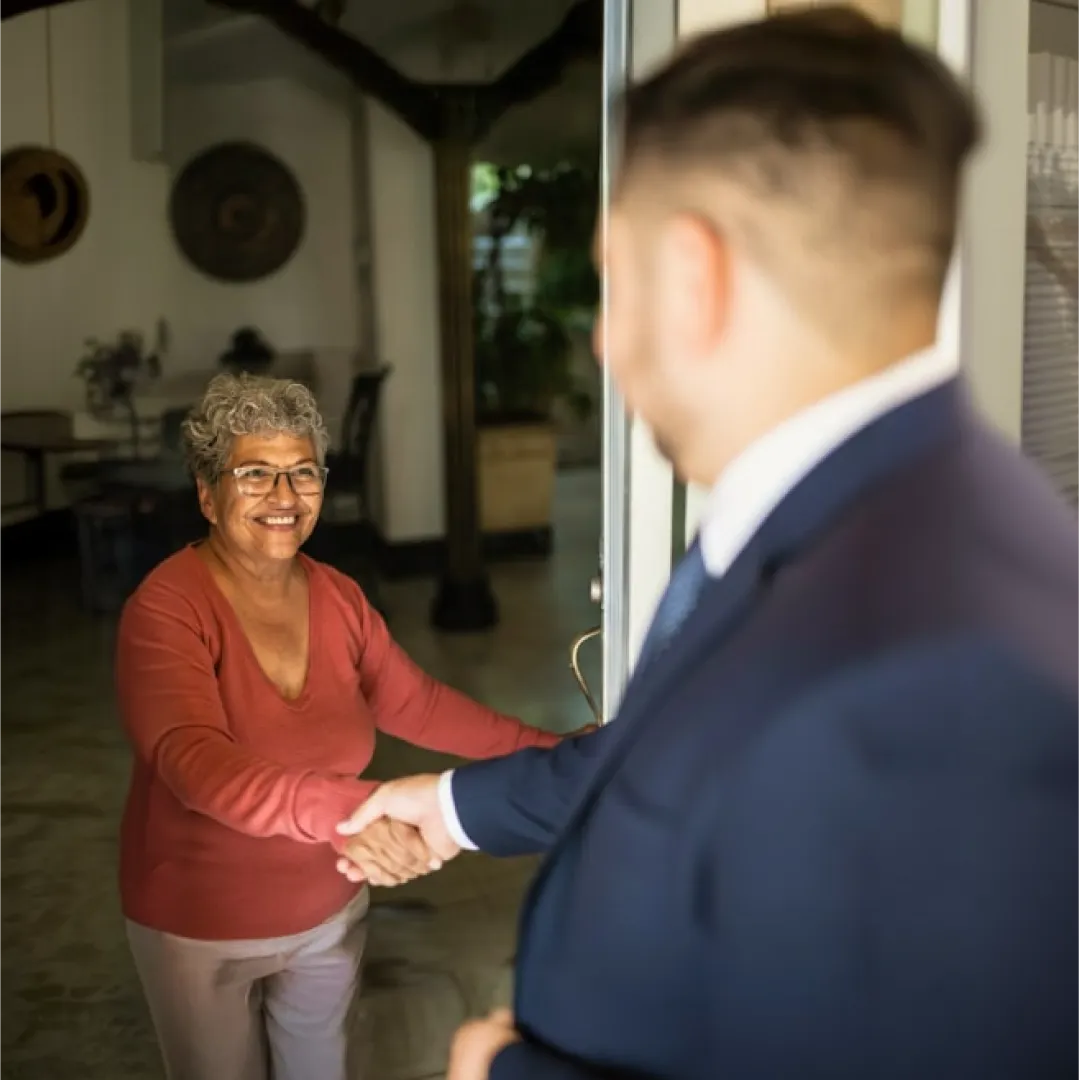 Persona adulta estrechando la mano de un asesor en la entrada de una vivienda, representando confianza, atención personalizada y acompañamiento en soluciones financieras de Banamex.